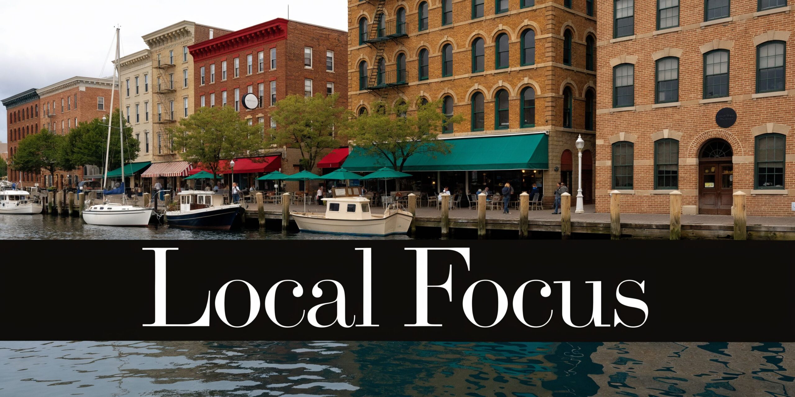 A scenic waterfront street featuring historic brick buildings, boats docked at a pier, and outdoor restaurant seating.